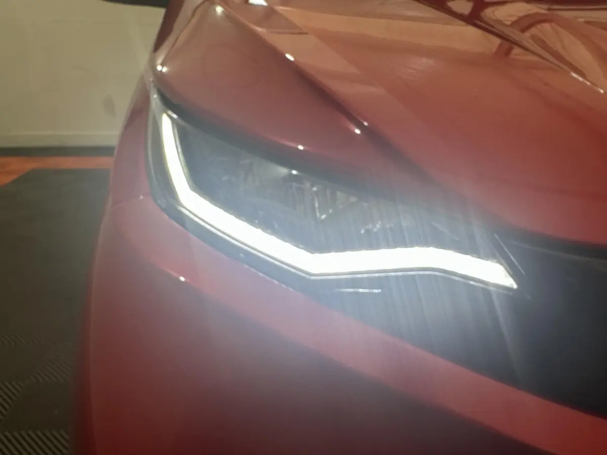 Gros plan sur le phare avant gauche allumé d’une Aixam Ambition 0.5 City Sport rouge, année 2026.