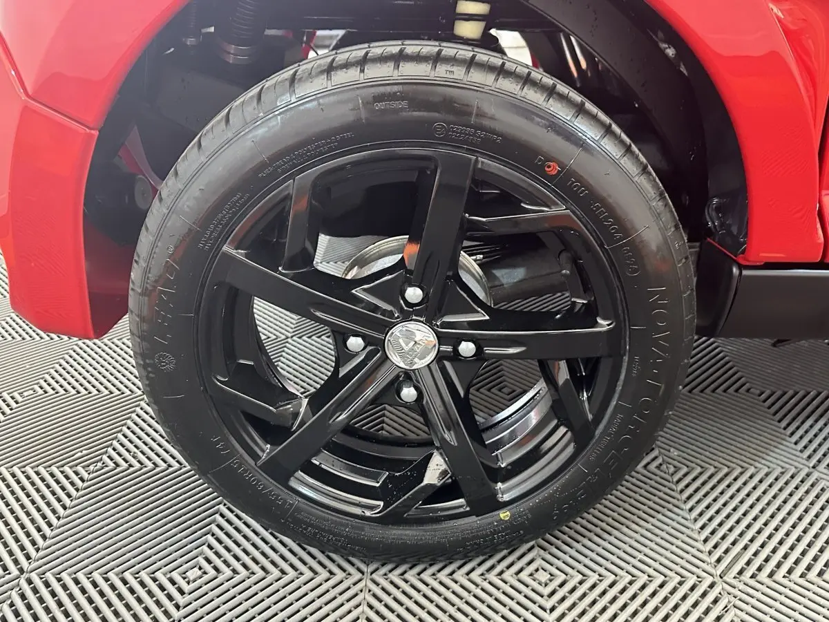 Gros plan sur la roue avant droite noire d’une Aixam Ambition 0.5 City Sport rouge, avec partie de la carrosserie visible.