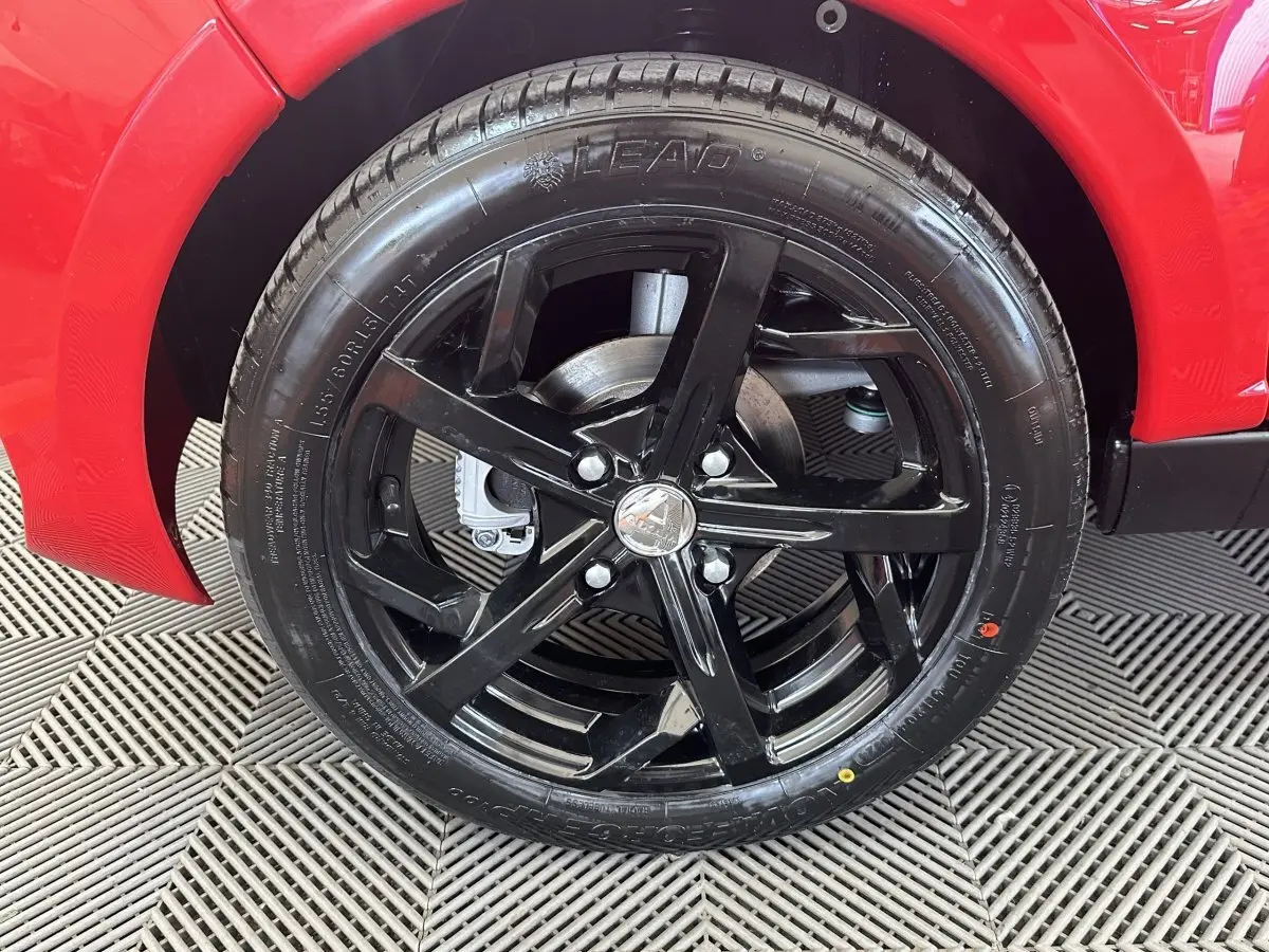 Gros plan sur la roue avant droite noire brillante d'une Aixam Ambition 0.5 City Sport rouge.