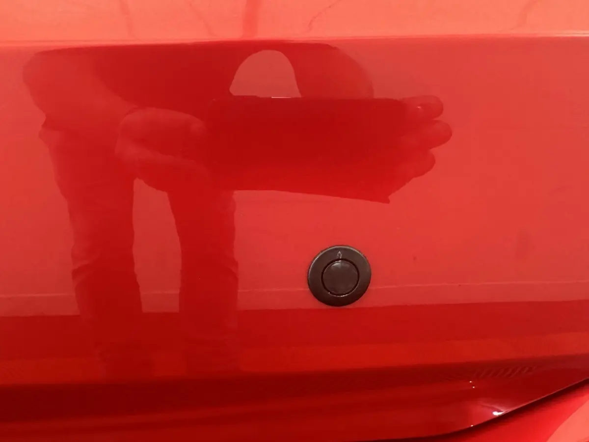 Détail du verrouillage de coffre sur la carrosserie rouge d'une Aixam Ambition 0.5 City Sport, vue rapprochée.