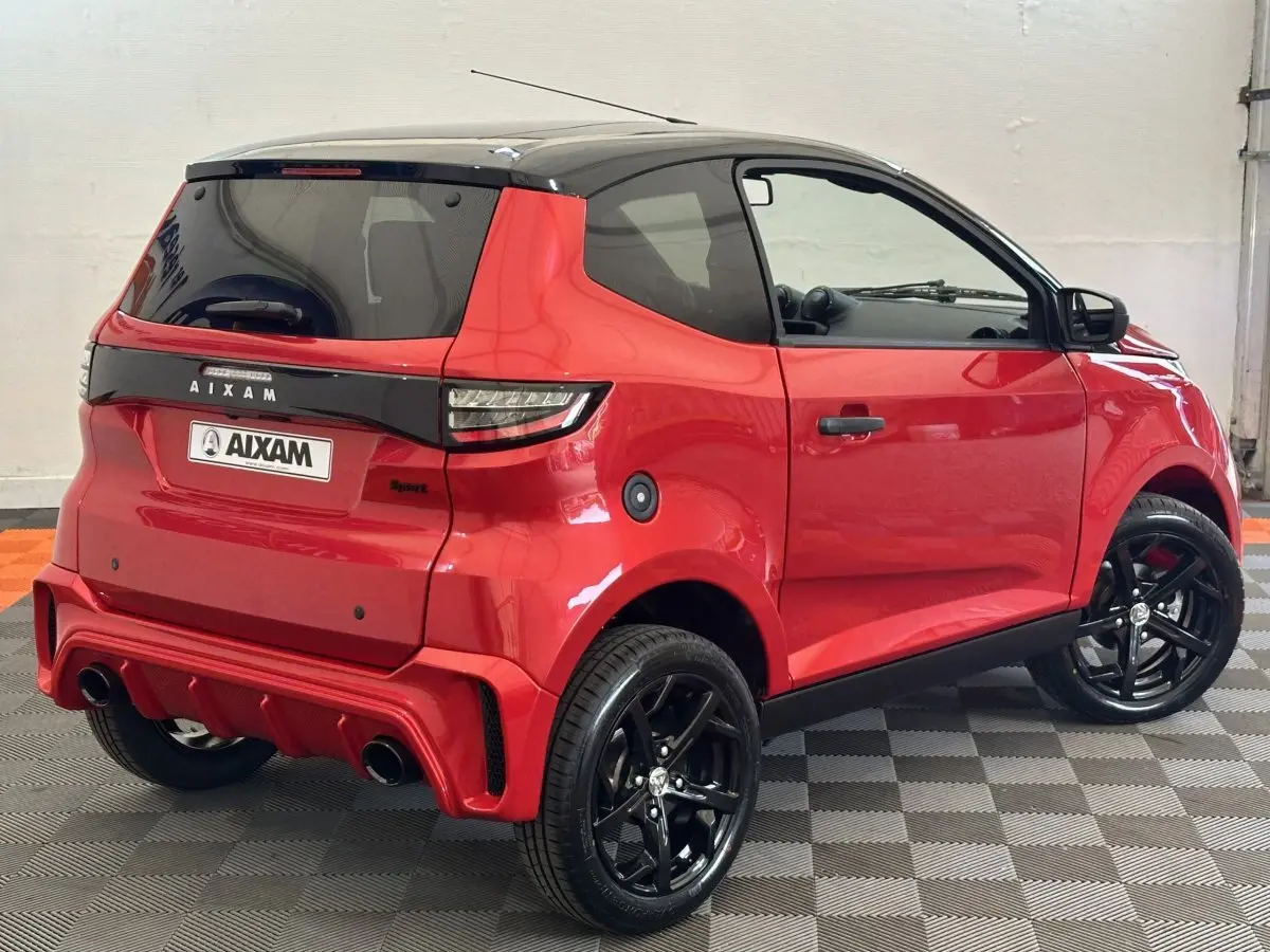 Vue 3/4 arrière droite d'une Aixam Ambition 0.5 City Sport rouge avec jantes noires et rétroviseur caméra côté gauche.