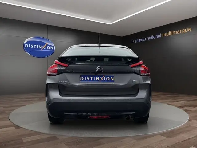 Vue arrière d'une Citroën C4 gris platinium 2022 avec feux LED et logo Distinxion sur fond intérieur showroom.
