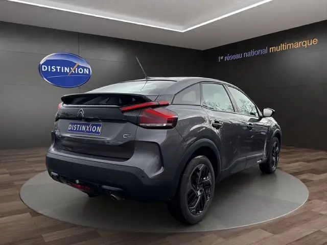 Vue 3/4 arrière droite d'une Citroën C4 gris platinium 2022 avec feux LED et jantes noires en showroom.