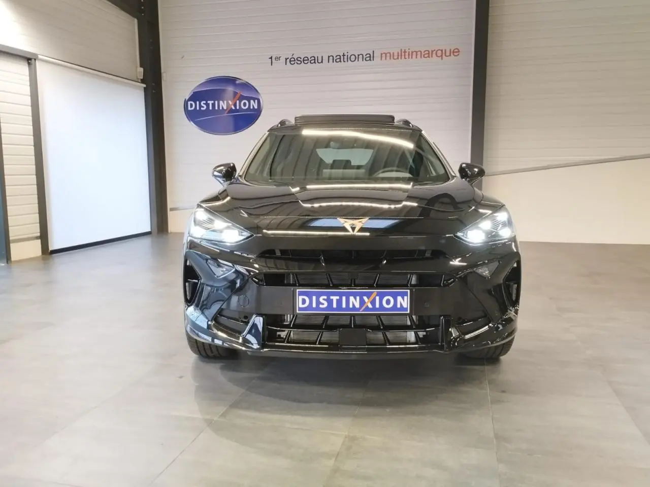 Vue frontale d'une CUPRA Formentor noire métal avec phares allumés et logo CUPRA lumineux au centre du capot.