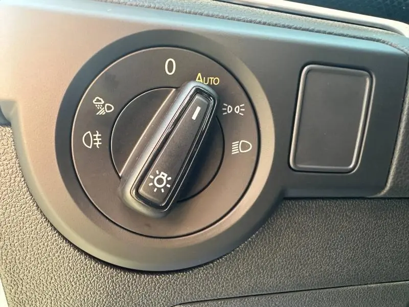 Gros plan sur le sélecteur de phares noir du Volkswagen T-Cross 2026, avec mode automatique activé, sur tableau de bord gris.