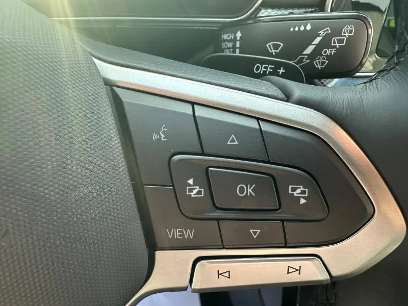 Gros plan sur les commandes multifonctions à gauche du volant cuir d’un Volkswagen T-Cross argenté, avec levier d’essuie-glace visible.