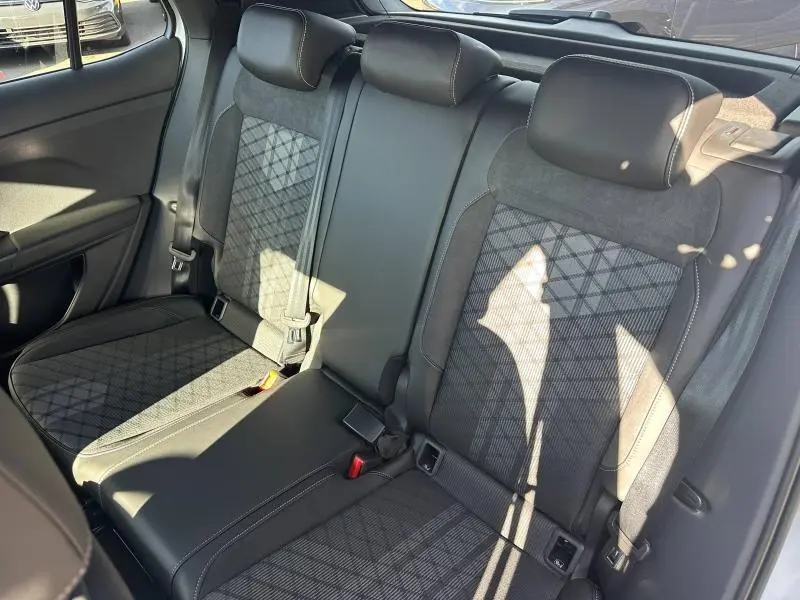 Vue intérieure arrière du Volkswagen T-Cross 2026, sièges tissu R-Line gris/noir avec motifs géométriques et appuie-têtes.