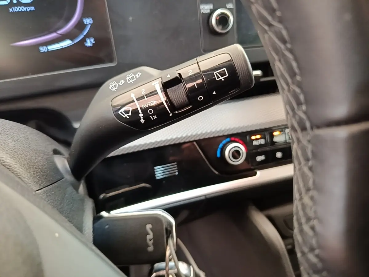 Gros plan sur la commande d’essuie-glace à gauche du volant du Kia Sportage beige, avec tableau de bord et climatisation visibles.
