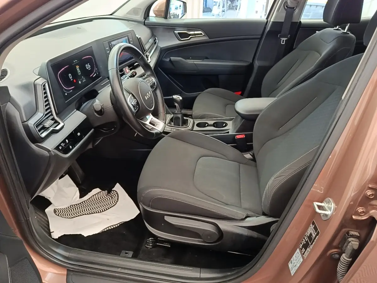 Vue intérieure côté conducteur du Kia Sportage beige 2022, avec sièges noirs, volant cuir multifonctions et tableau de bord digital.