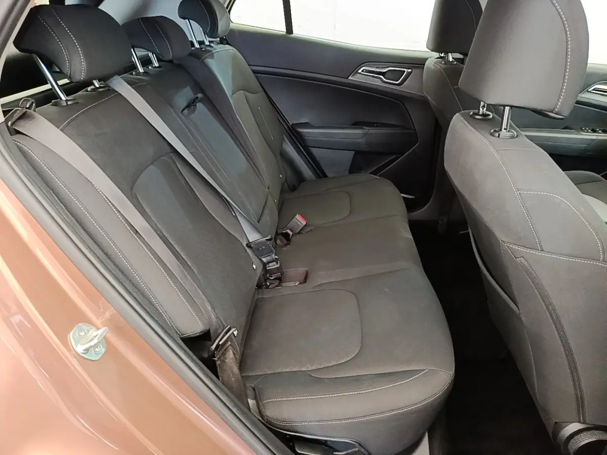Vue intérieure côté arrière gauche du Kia Sportage beige 2022 montrant la banquette arrière en tissu gris foncé avec ceintures de sécurité.