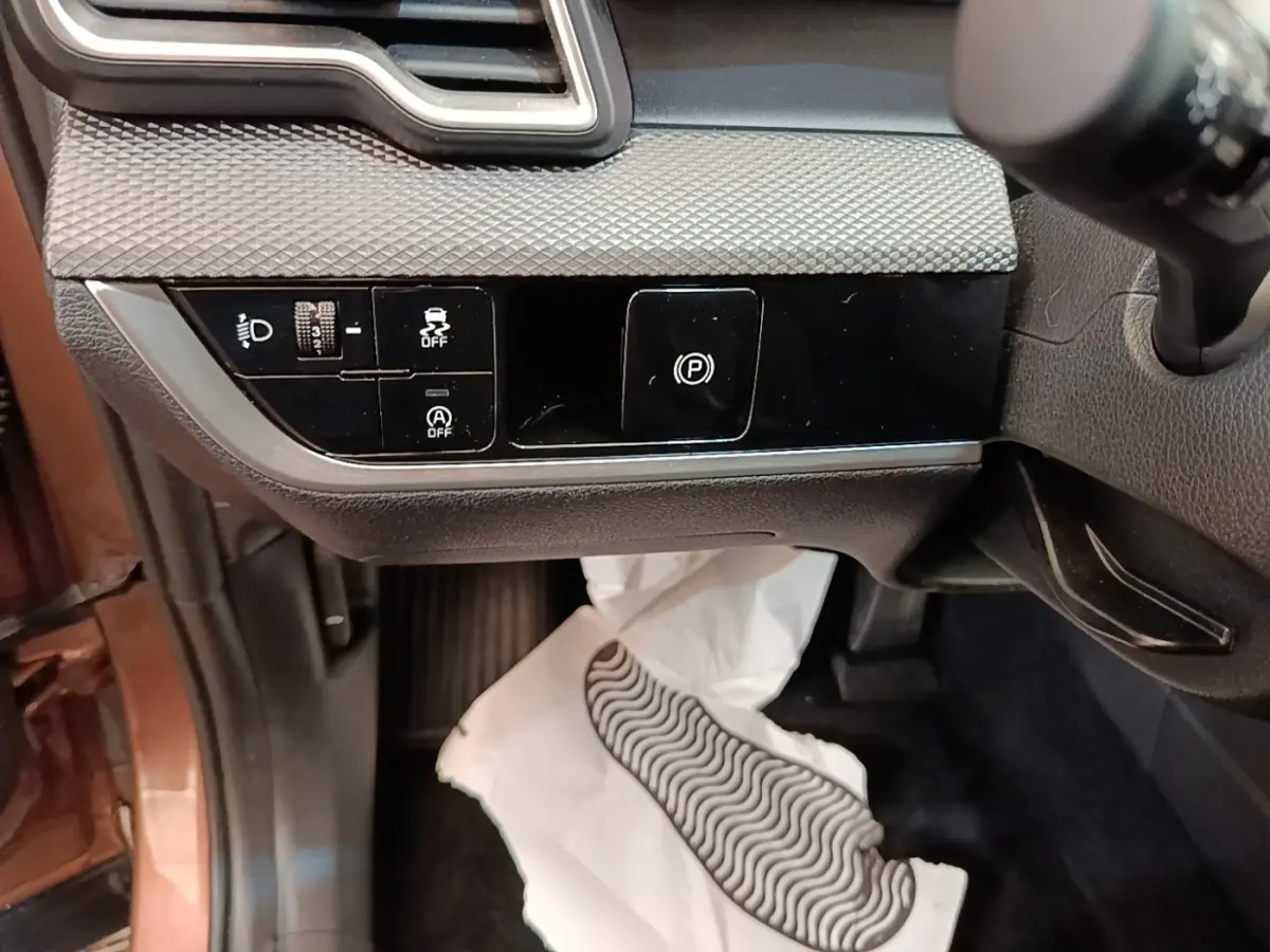Détail intérieur côté gauche du tableau de bord beige du KIA SPORTAGE 2022 avec commandes d’éclairage et frein à main électrique.