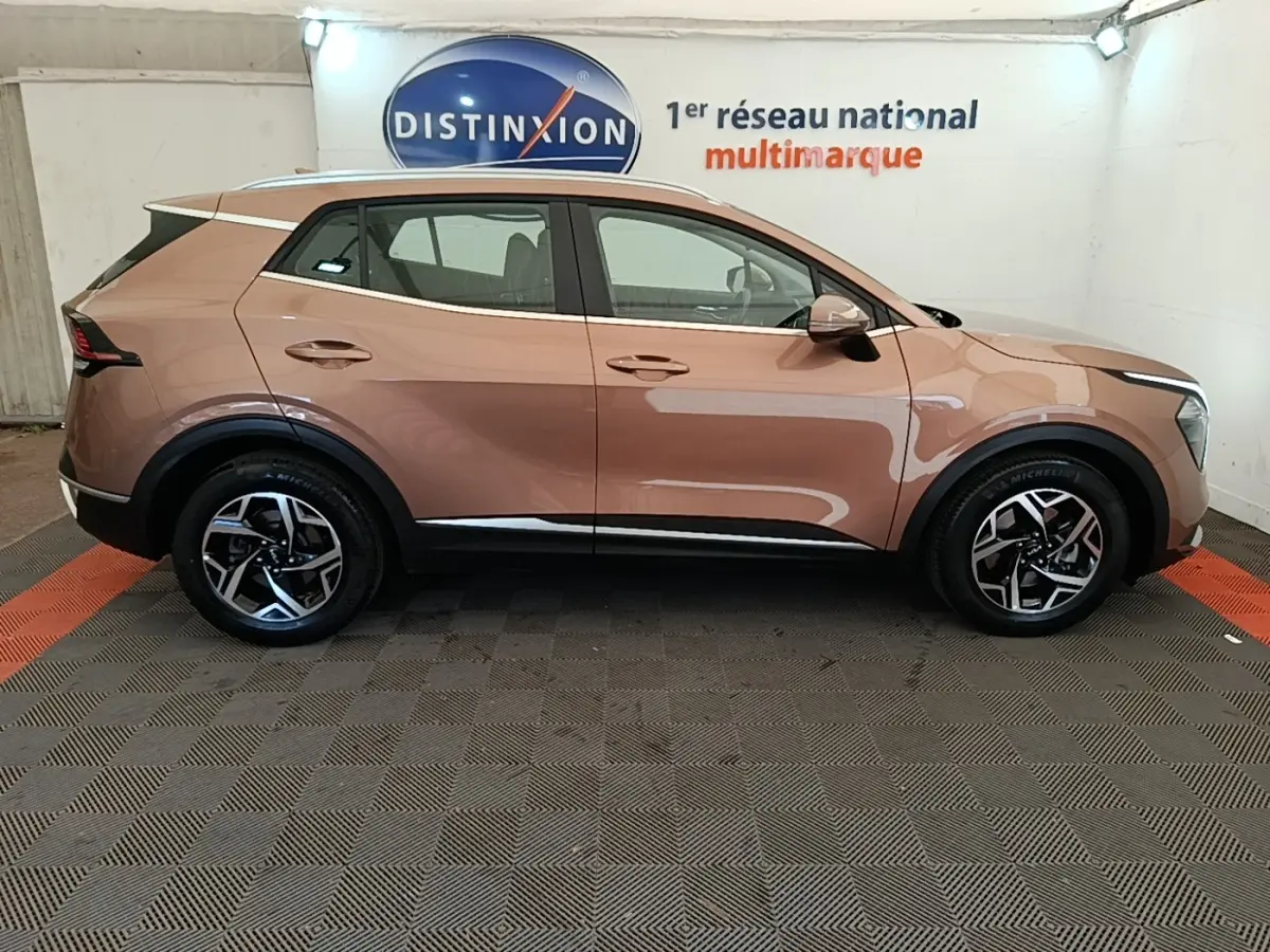 Profil droit d'un KIA SPORTAGE beige 2022 avec jantes alliage et rétroviseurs électriques dans un showroom.