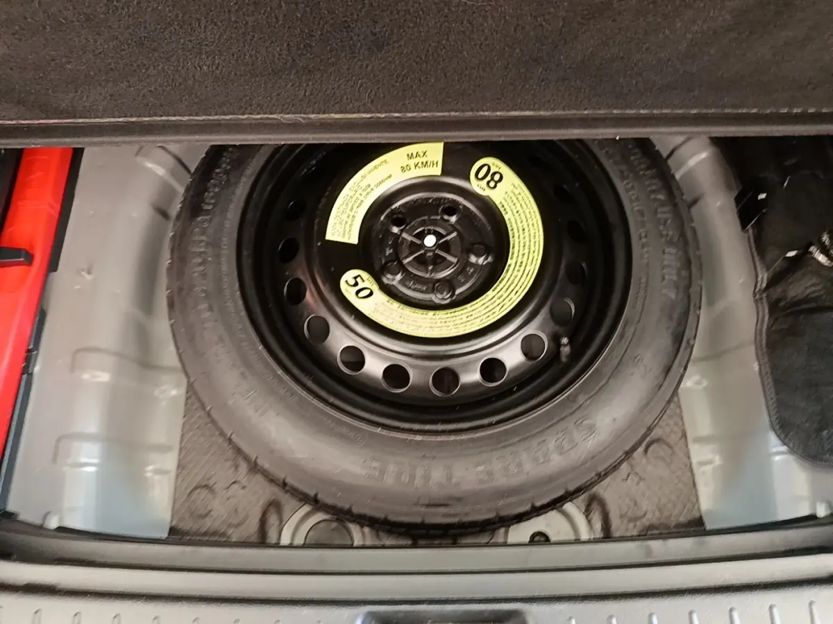 Roue de secours compacte noire visible dans le coffre d’un KIA SPORTAGE beige, vue en plongée.