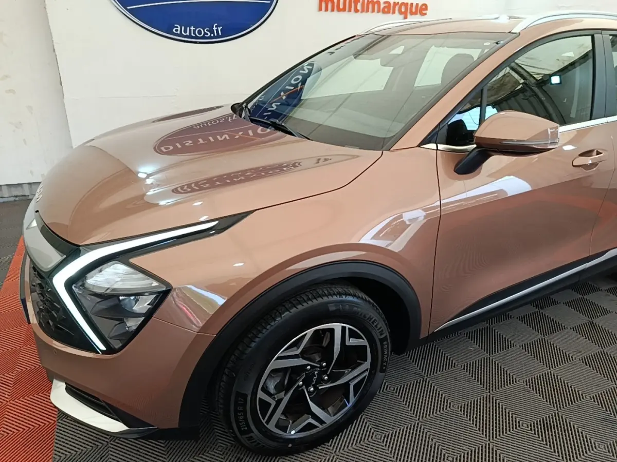 Vue 3/4 avant droit d’un Kia Sportage beige 2022 avec phares LED en forme de boomerang et jantes alliage noires.
