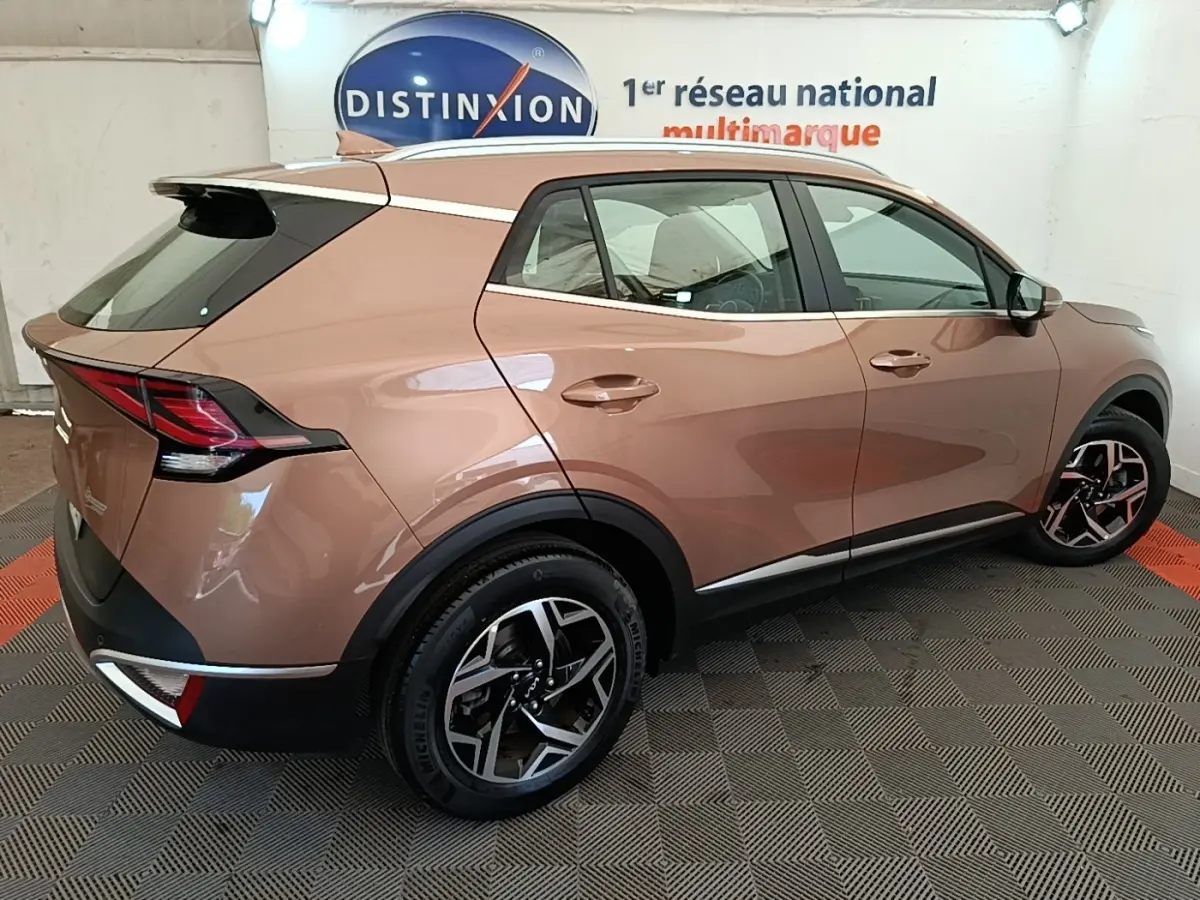 KIA Sportage beige vue 3/4 arrière droit, avec jantes alliage et feux arrière LED distinctifs.