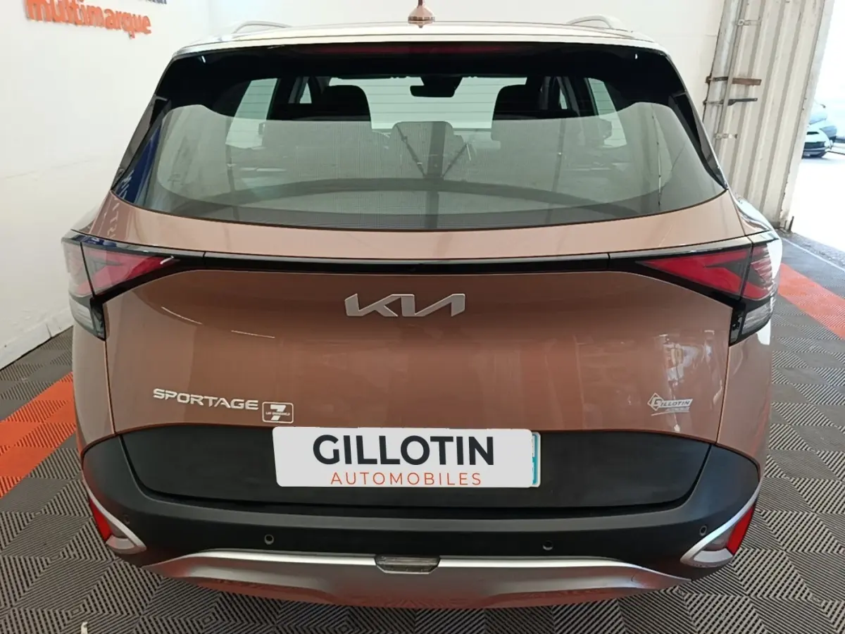 Vue arrière d’un KIA Sportage beige 2022 avec feux arrière LED et logo moderne sur hayon.