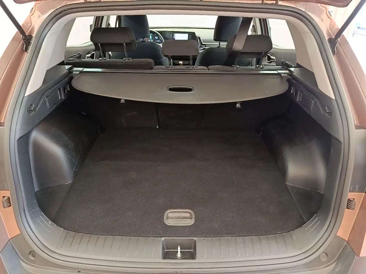 Coffre ouvert vu de l'arrière d'un KIA SPORTAGE beige 2022, avec cache-bagages et banquette arrière rabattable.