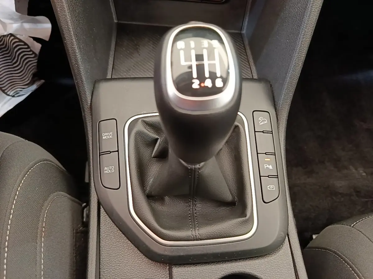 Gros plan sur le levier de vitesses manuel noir du Kia Sportage beige, entouré de boutons de contrôle sur la console centrale.