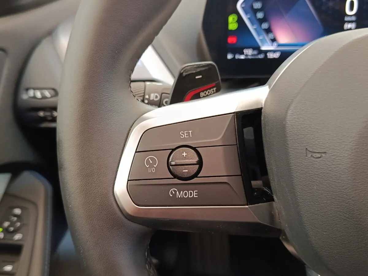 Gros plan sur les commandes à gauche du volant cuir noir de la BMW Série 1 120 DKG7 M Sport 2025.