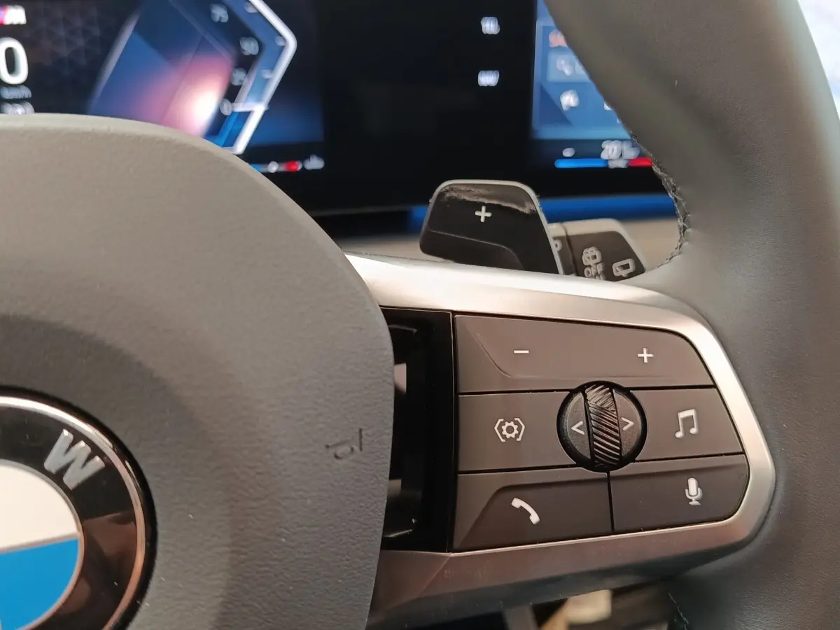 Gros plan sur les commandes multifonctions à droite du volant cuir gris d’une BMW Série 1 120 DKG7 M Sport 2025.