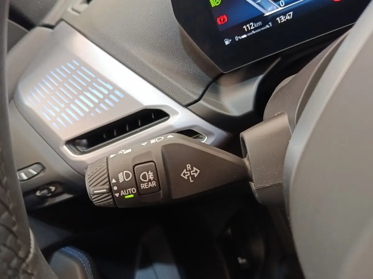 Gros plan sur la commande des feux et clignotants dans l’habitacle d’une BMW Série 1 gris clair, affichage numérique partiel visible.