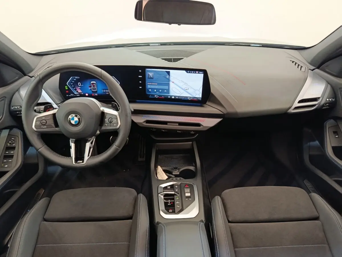 Vue intérieure avant de la BMW Série 1 120 DKG7 M Sport 2025, tableau de bord noir avec écran tactile large et volant cuir.