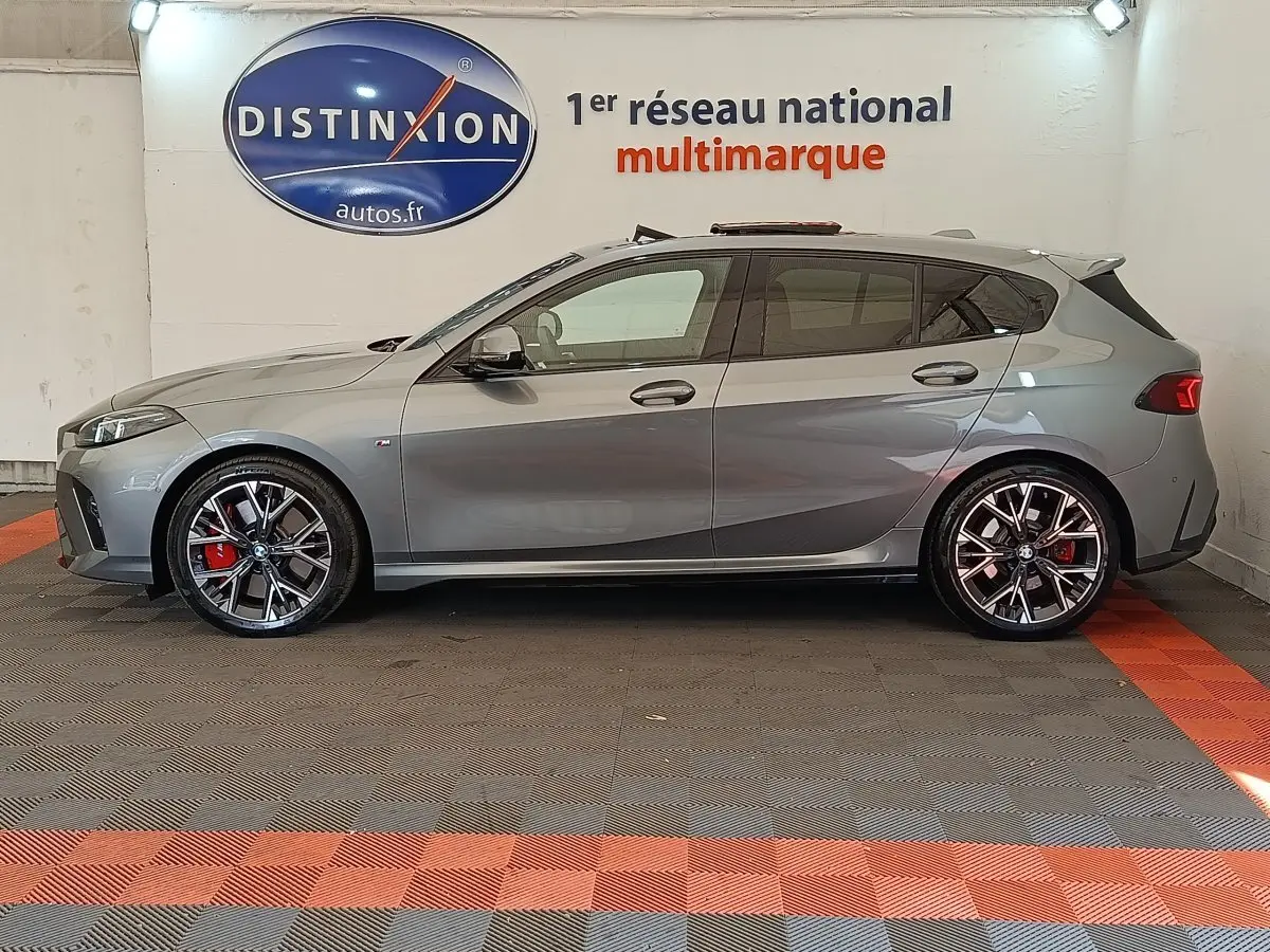 BMW Série 1 120 DKG7 M Sport gris clair vue de profil côté gauche avec jantes sport et étriers rouges visibles.