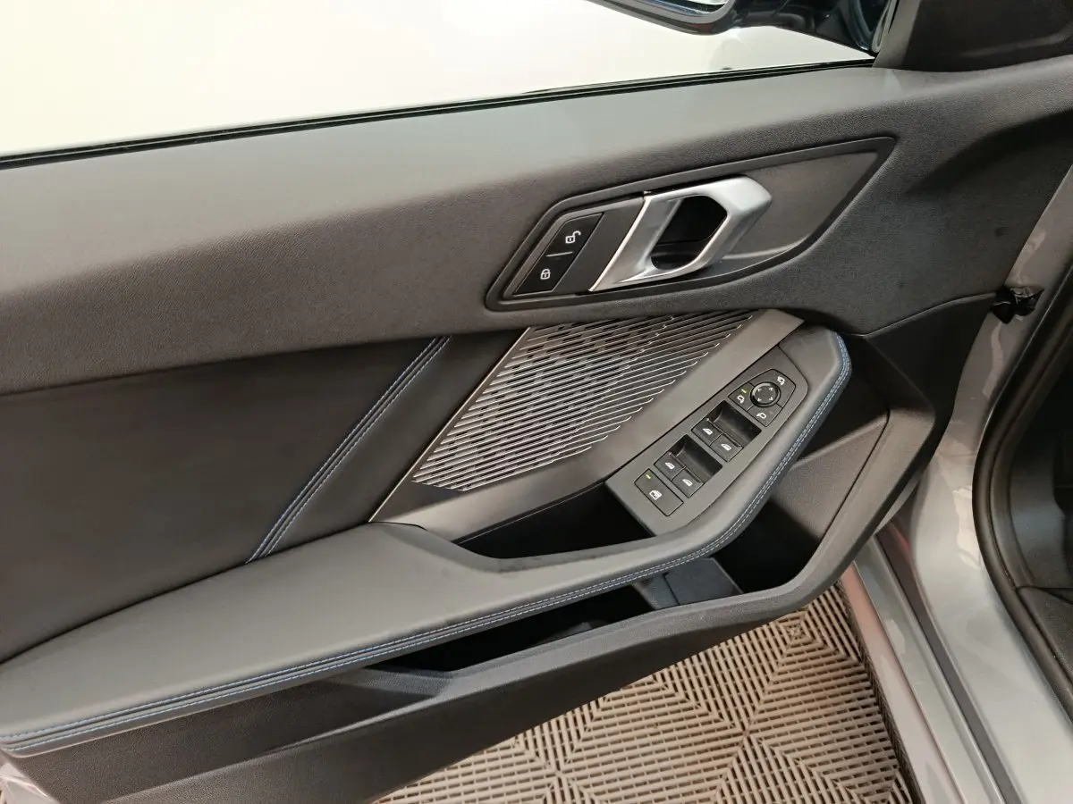 Vue rapprochée de la porte avant gauche grise d’une BMW Série 1 120 DKG7 M Sport avec commandes de vitres et serrure.