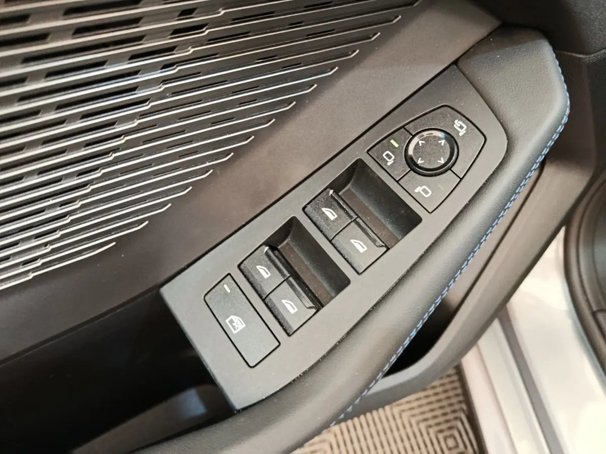 Gros plan sur les commandes des vitres et rétroviseurs côté conducteur d’une BMW Série 1 gris clair, intérieur noir avec surpiqûres bleues.