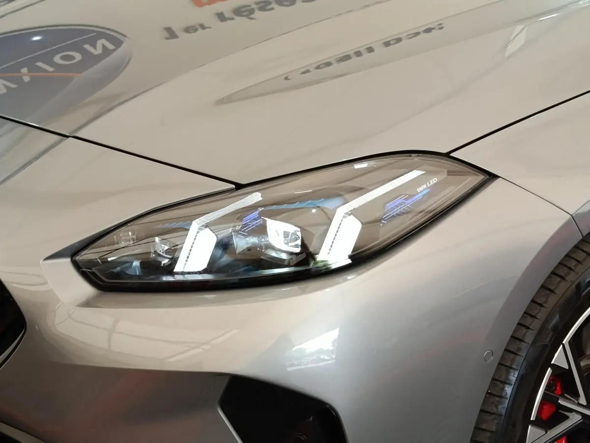 Gros plan sur le phare avant droit LED d’une BMW Série 1 gris clair avec jante sport et étrier rouge visible.