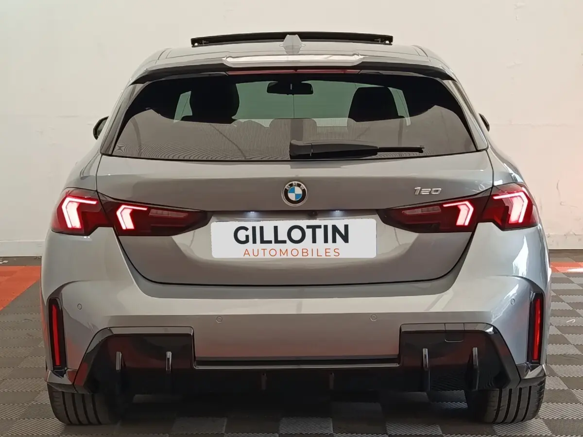 Vue arrière d'une BMW Série 1 120 DKG7 M Sport gris clair avec feux LED allumés et diffuseur noir sportif.