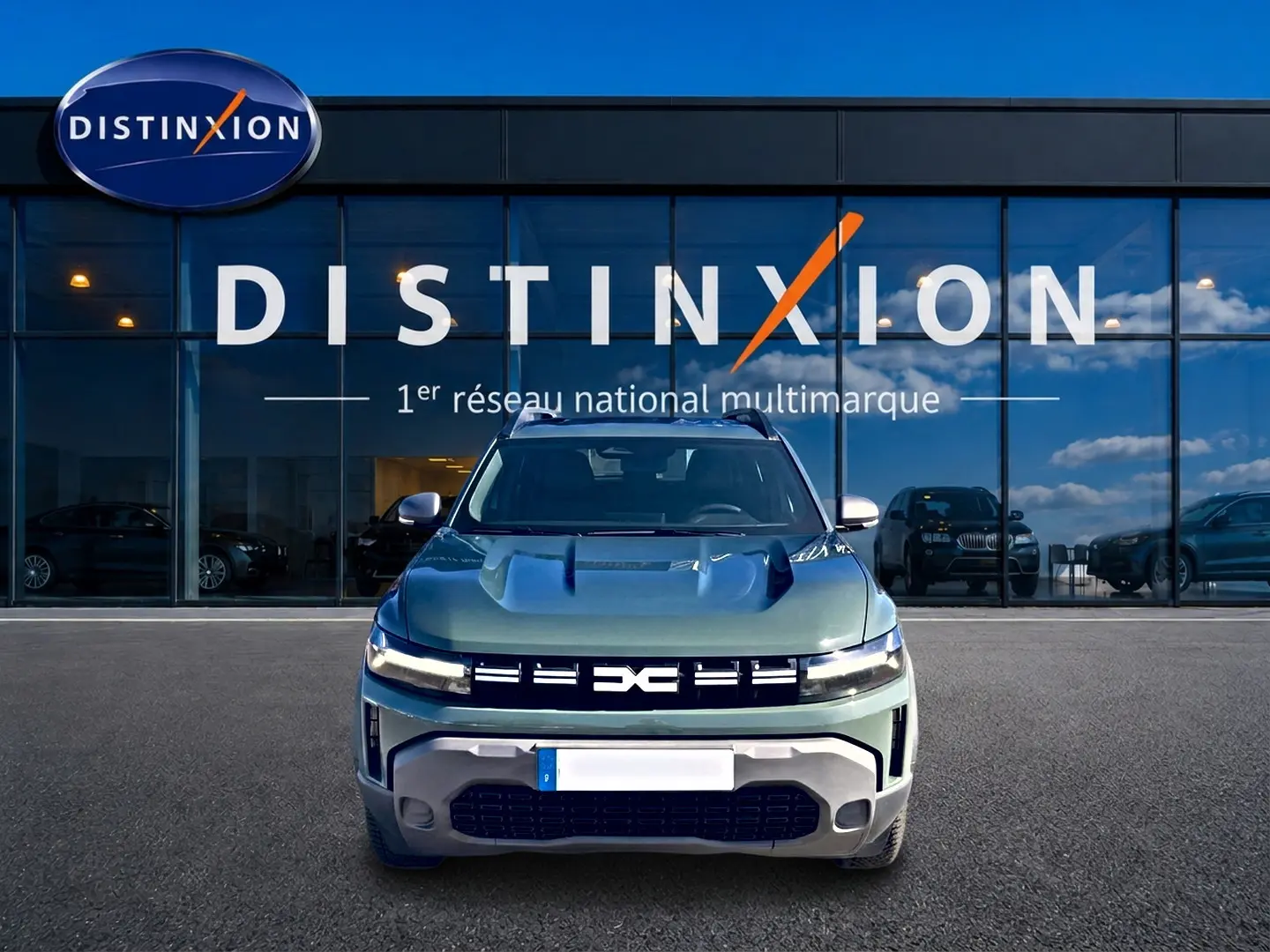 Vue frontale d'un Dacia Duster 1.2 hybrid-g 150 expression 4x4 en kaki lichen devant une vitrine Distinxion.