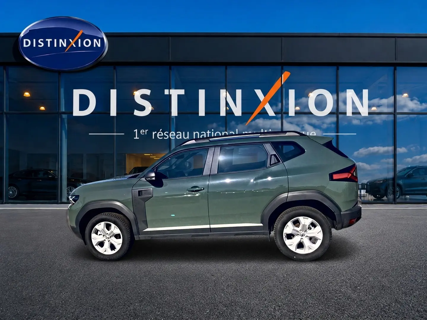 Profil droit du Dacia Duster 2026 kaki lichen avec barres de toit et jantes alu devant une vitrine Distinxion.