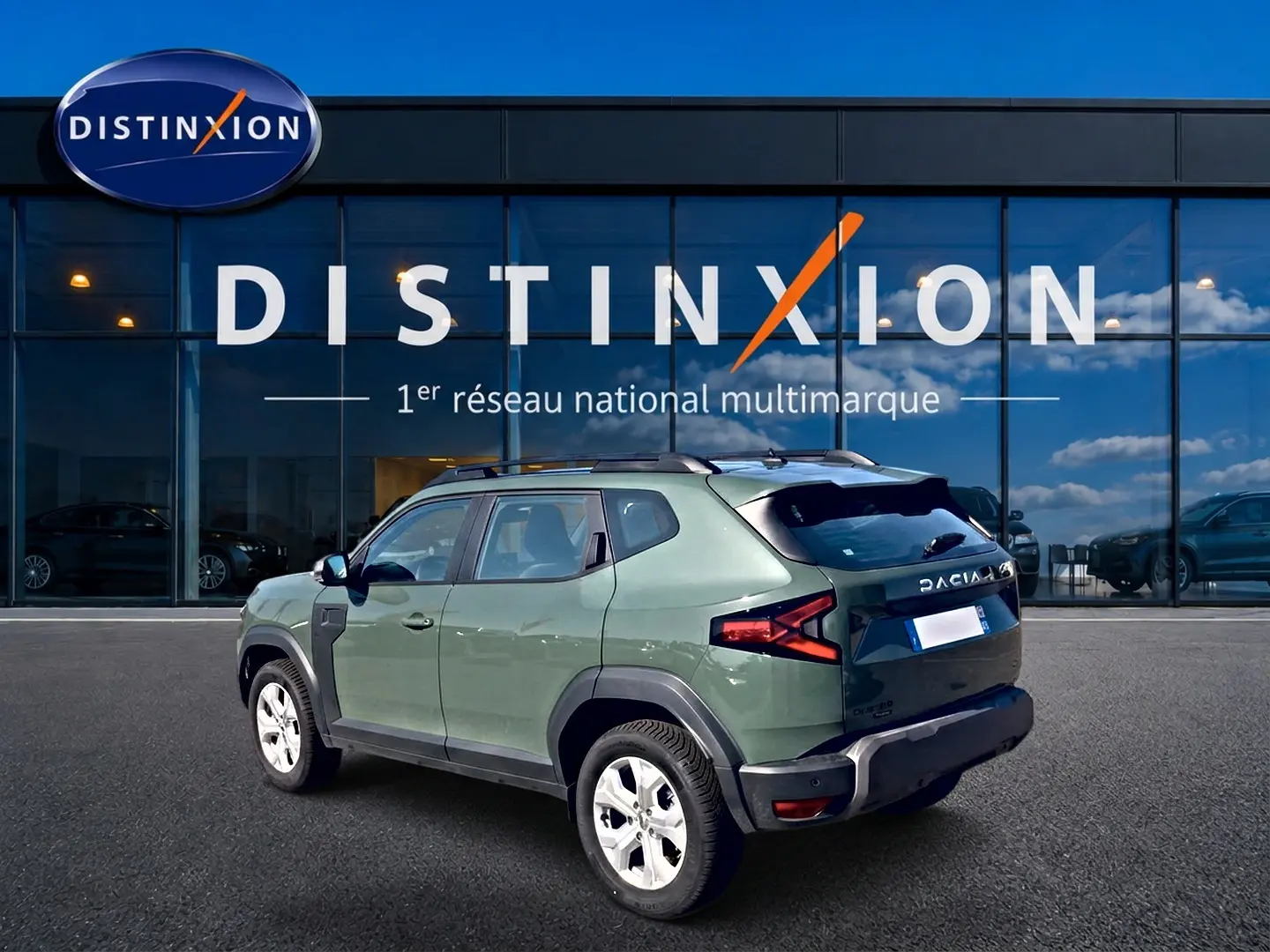 Dacia Duster 1.2 hybrid-g 150 expression 4x4 kaki lichen vu en 3/4 arrière droit devant un showroom Distinxion.