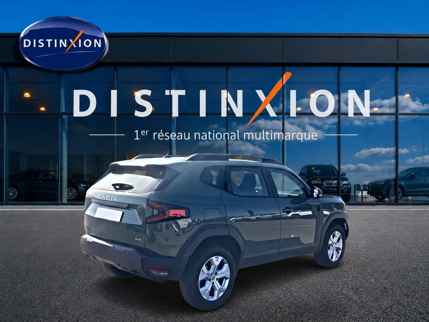 Vue 3/4 arrière droite d'un Dacia Duster 2026 kaki lichen avec barres de toit et jantes alu devant un showroom Distinxion.
