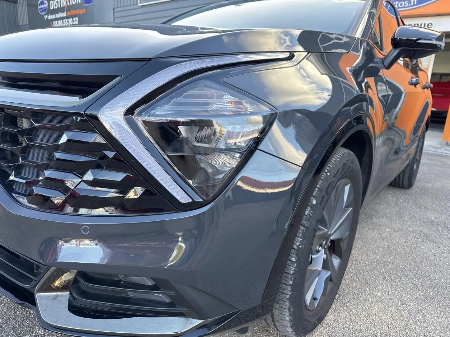 Gros plan sur l'avant droit du Kia Sportage gris Eclipse Métallisée, mettant en valeur le phare et la calandre distinctive.