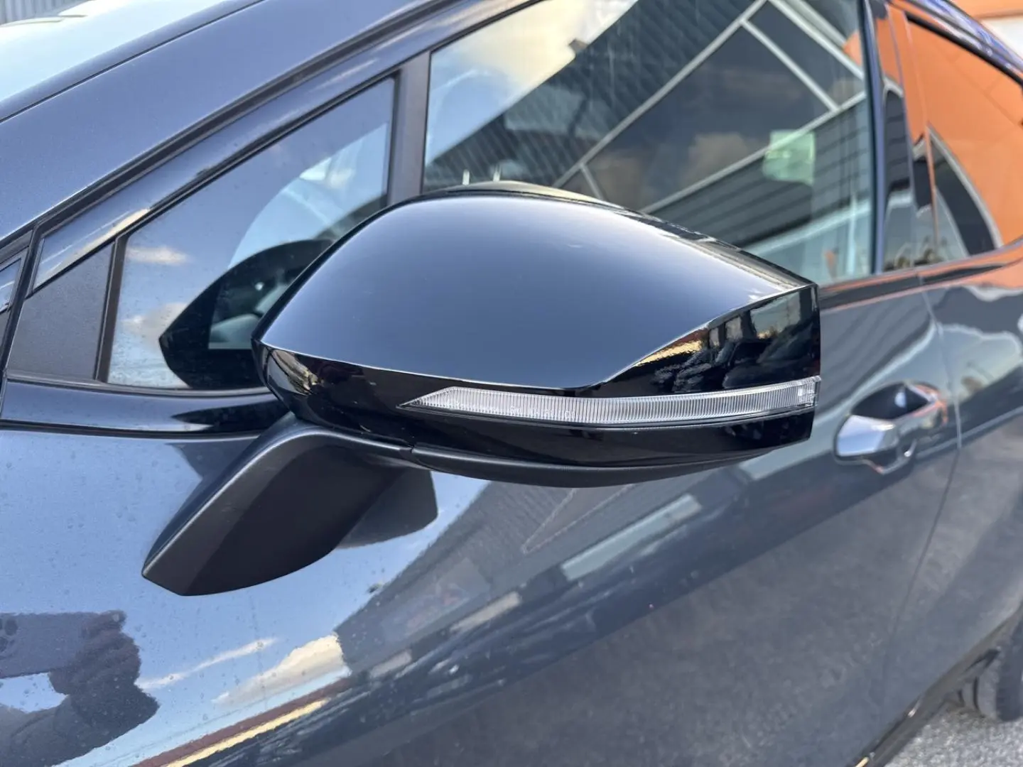 Rétroviseur noir brillant avec clignotant intégré sur le côté gauche d’un KIA Sportage gris Eclipse Métallisée.