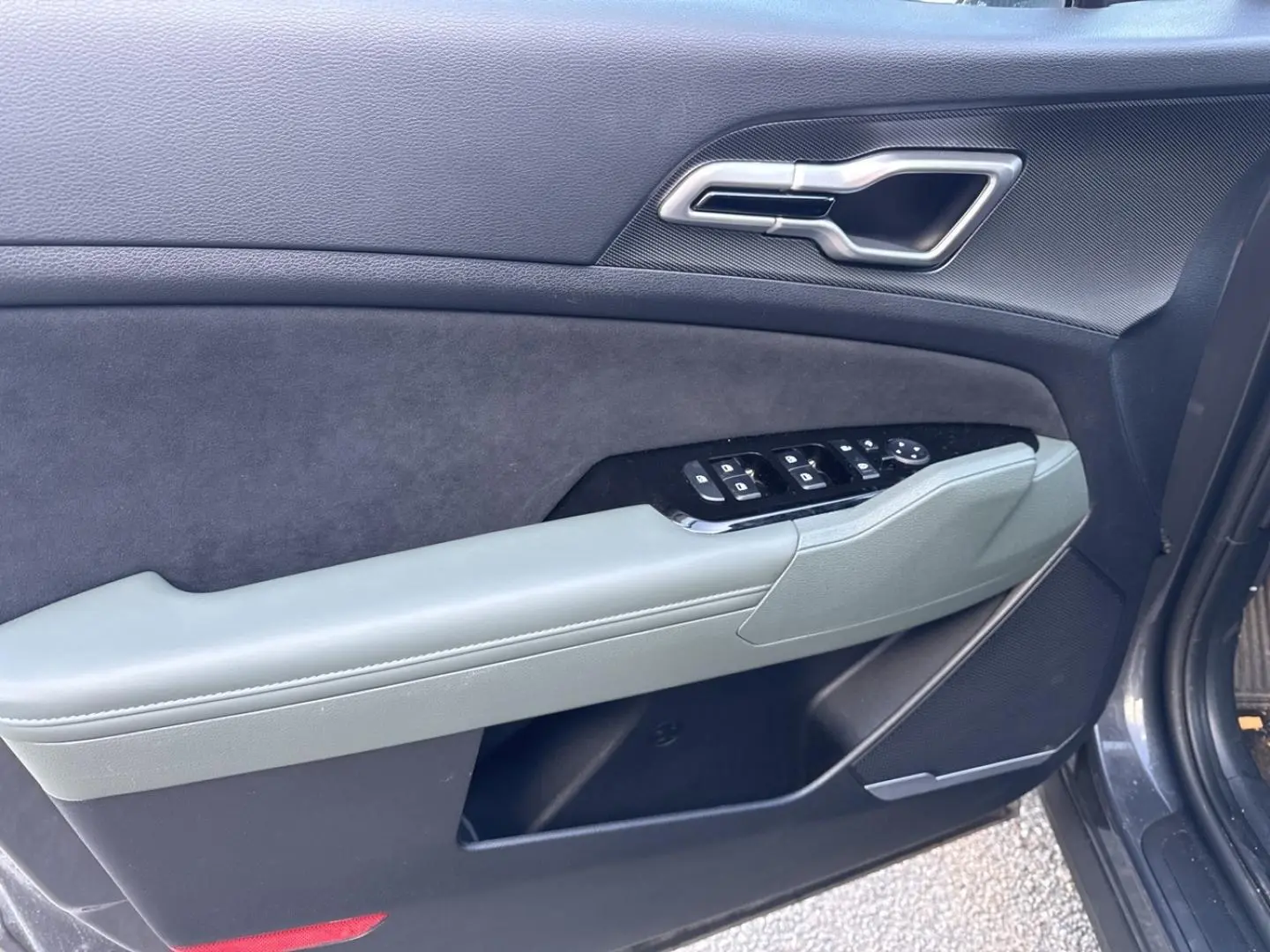 Vue rapprochée de la porte avant gauche du KIA SPORTAGE gris Eclipse Métallisée avec commandes de vitres et poignée intégrée.