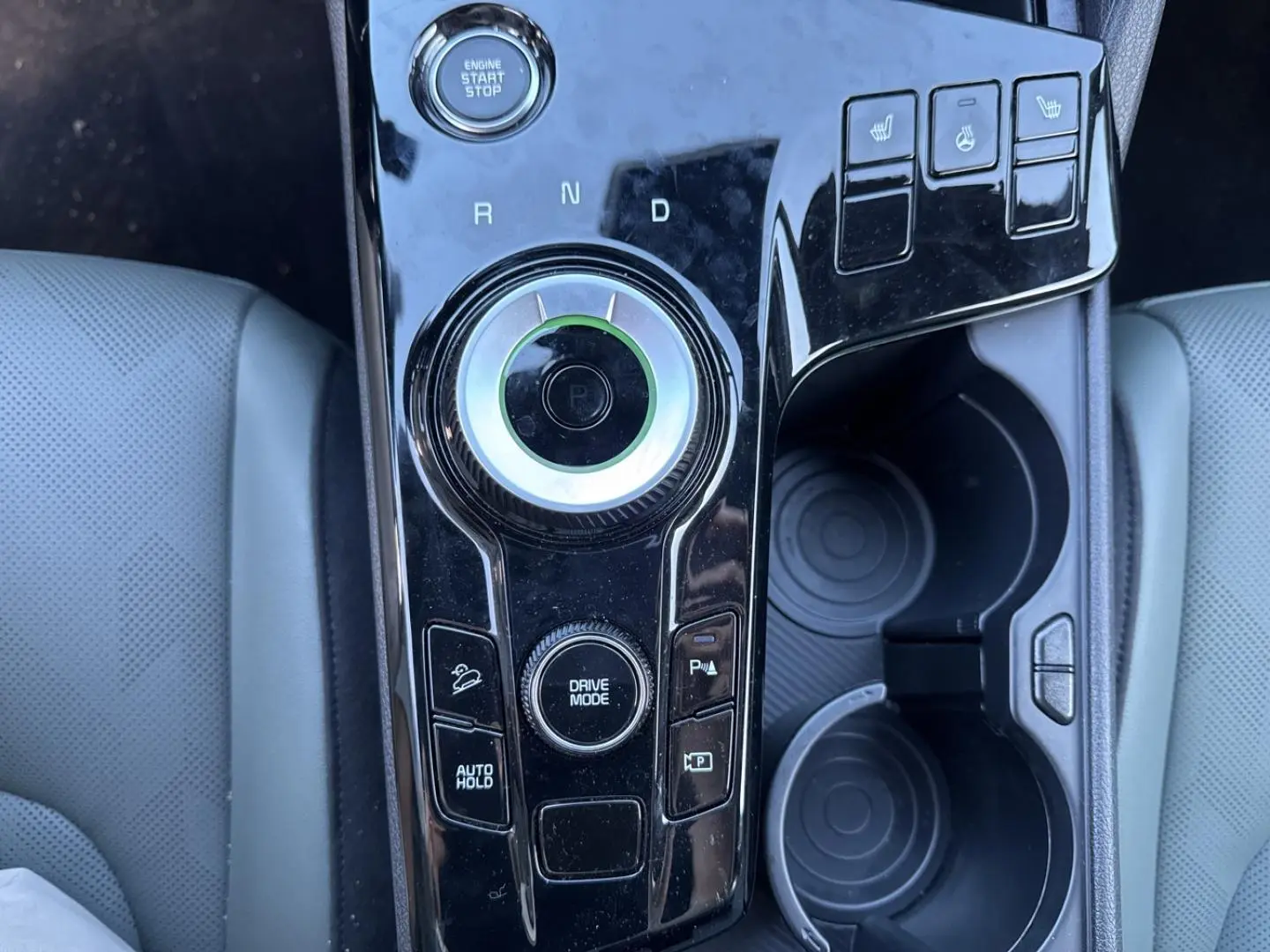 Vue plongeante sur la console centrale noire brillante du Kia Sportage gris, avec sélecteur rotatif et boutons chauffants.
