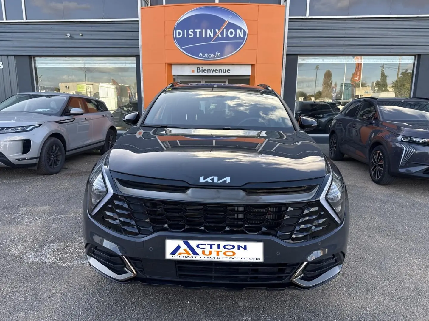 Vue avant d'un Kia Sportage 2025 gris Eclipse métallisé avec calandre noire et phares LED, devant un concessionnaire.