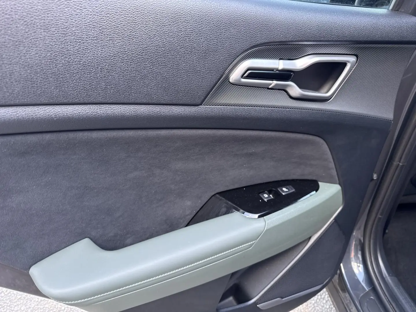 Vue rapprochée de la porte avant gauche du KIA Sportage gris Eclipse avec accoudoir vert pin et commandes de vitres.