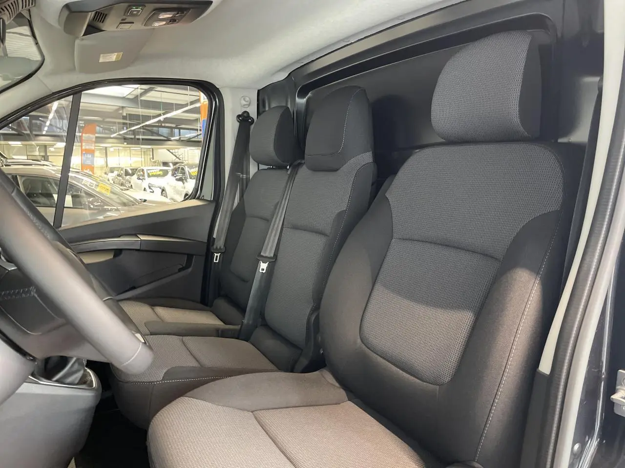 Intérieur du Renault Trafic Fourgon gris Comète, vue côté conducteur montrant les sièges avant en tissu noir.