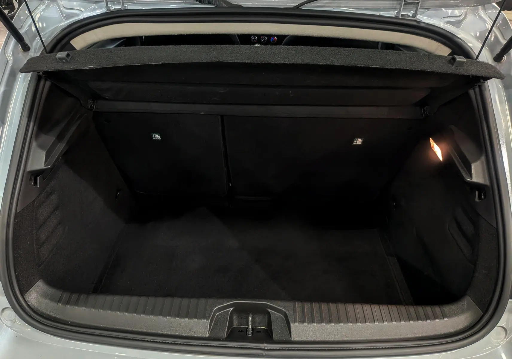 Coffre ouvert vu de l'arrière d'une Renault Clio V Gris Rafale, montrant l'espace de chargement vide et l'éclairage intérieur.