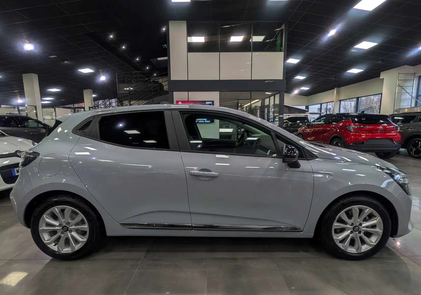 Profil côté gauche de la Renault Clio V 2025 gris Rafale en intérieur, soulignant ses jantes alliage et lignes épurées.