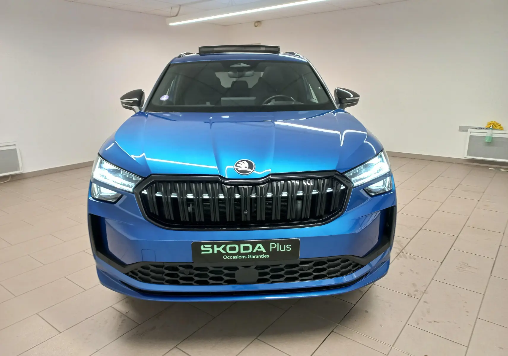 Vue frontale d'un Skoda Kodiaq 1.5 TSI 150 DSG7 Sportline en bleu RS avec calandre noire et toit panoramique.