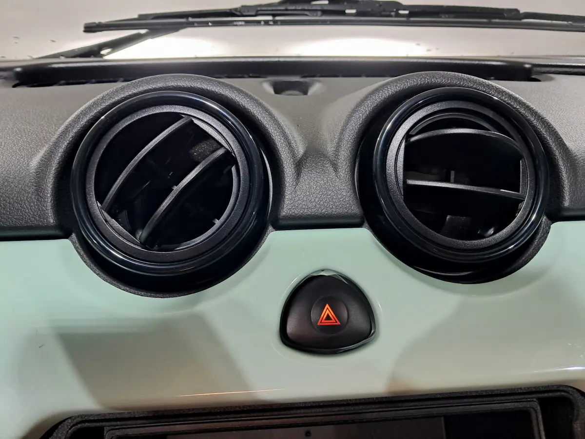 Détail du tableau de bord vert de l'AIXAM MINAUTO E chic 2026 avec deux aérateurs ronds et bouton de warning central.