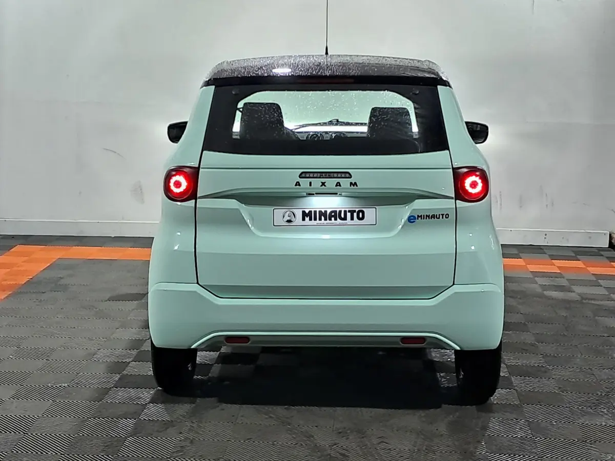 Vue arrière d'une AIXAM MINAUTO E chic 2026 électrique vert clair avec feux ronds allumés et toit noir.
