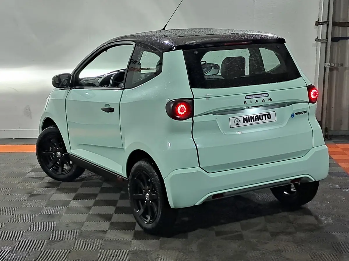 Vue 3/4 arrière droite de l'AIXAM MINAUTO E chic 2026 vert clair avec toit noir et feux arrière allumés.