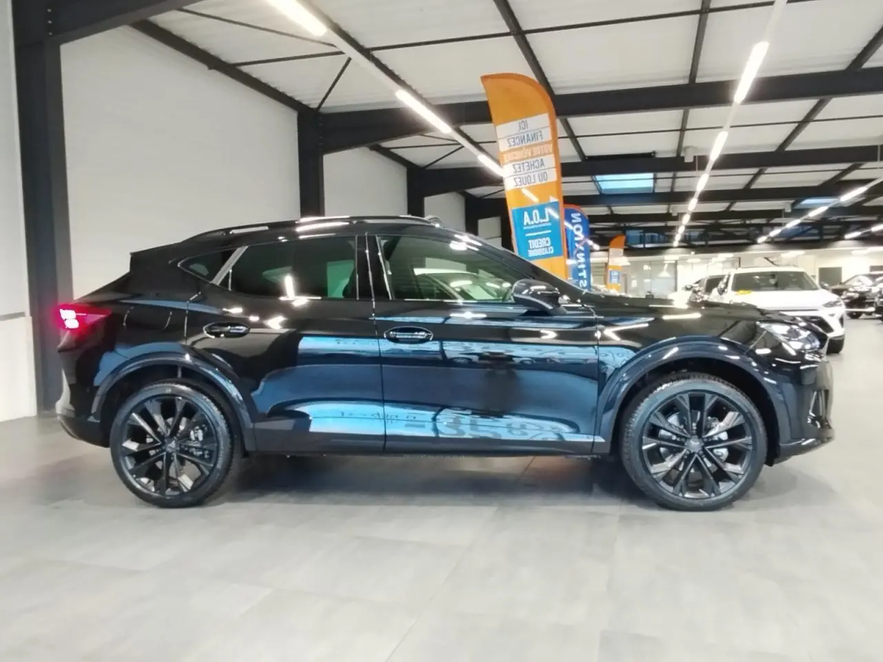 Profil droit du CUPRA Formentor noir métal 2026 avec jantes alliage noires et toit ouvrant panoramique visible en intérieur showroom.