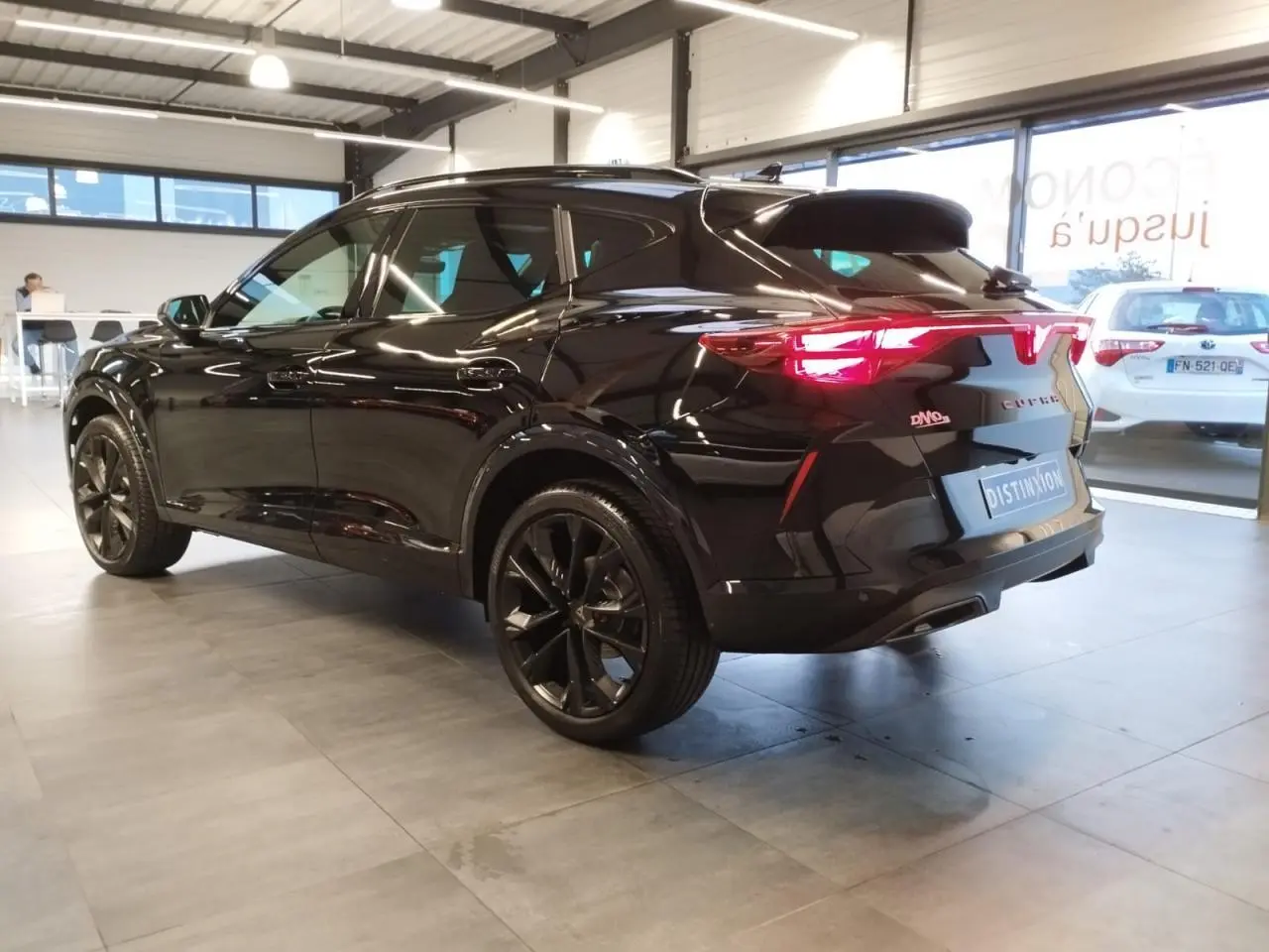 Vue 3/4 arrière droite d'une CUPRA Formentor noire métal avec jantes alliage noires et feux arrière Tri-LED allumés.